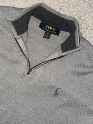   Ralph Lauren - Snygg grå tröja från Polo Ralph Lauren med halv dragkedja och broderad logga på bröstet. Tröjan har ribbade muddar och krage med mörkare grå insida. Perfekt för en stilren och avslappnad look. Pris kan diskuteras 