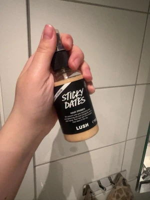 Lush Sticky Dates Hair Primer - Sticky Dates Hair Primer från Lush i en praktisk plastflaska med sprayfunktion. Produkten är ljusbeige och används för att förbereda håret inför styling. Doftar sött och är perfekt för dig som vill ha extra vård och glans till håret.