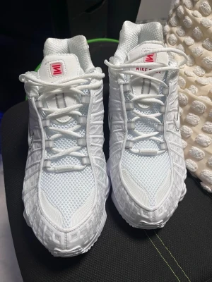 Vita Nike x Martine Rose sneakers - Säljer ett par vita Nike x Martine Rose sneakers med cool mesh och detaljer i syntet. Skorna har röda loggor på plösen och innersulan, samt klassisk snörning. Perfekta för dig som gillar stilrena och unika sneakers med modern vibe.
