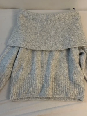 Ljusgrå off shoulder stickad tröja H&M - Mysig ljusgrå stickad tröja från H&M med bred off shoulder-krage. Tröjan har ribbstickade detaljer och långa ärmar. Perfekt för kalla dagar när du vill vara både bekväm och snygg.