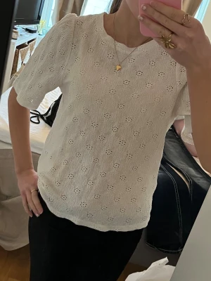 Vit blus med broderade blommor - Söt vit blus med korta ärmar och broderade blommor i tyget. Blusen har en rund halsringning och lätt puffade axlar för en trendig look. Perfekt att matcha med jeans eller kjol för en fräsch stil. Materialet känns luftigt och bekvämt.
