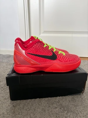Nike Kobe 6 Protro Grinch sneakers - Nike Kobe 6 Protro Grinch sneakers i rött med svart Swoosh och neongröna skosnören. Ovandelen har en texturerad, reptilinspirerad yta och Kobe-logga på plösen. Låg modell med syntetmaterial och mesh för bra andningsförmåga. Perfekta för basket eller streetwear. Köpta för ca 5000kr köpte dom i storlek 43 fick dom i 44 därför säljer jag vill ha sålt dom för jag ska köpa andra skor säljer för 999kr priset går o diskutera 