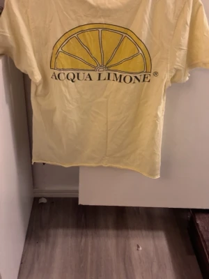 Gul Acqua Limone t-shirt - Snygg gul t-shirt från Acqua Limone med klassisk citronskiva och logga på ryggen samt tryck framtill. T-shirten har korta ärmar och är tillverkad i mjuk bomull, perfekt för en avslappnad och trendig stil. Köpt för 599kr men säljer den för 400kr eftersom den aldrig har använts ☺️ pris kan diskuteras 