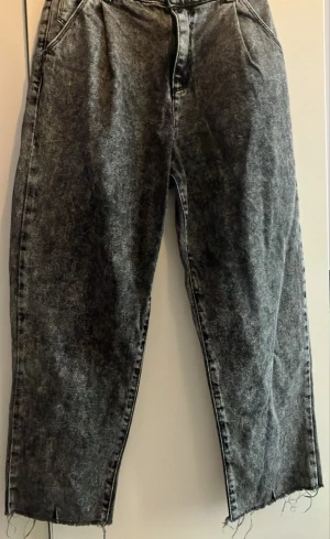 Grå tvättade mom jeans med rå kant - Säljer ett par grå mom jeans med tvättad look och råa, avklippta benslut. Jeansen har hög midja, fickor fram och bak samt avslappnad passform. Perfekta för en chill och trendig stil.