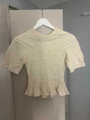 Gul smockad topp med volang/bluzka - Söt guk topp med smockad midja och volangkant nedtill. Kortärmad modell med rund halsringning och lätt rynkade detaljer. Perfekt för en trendig och feminin look. Den är mer gul i verkligheten än på kameran!!💕