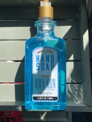 Blå handtvål i ginflaska-look - Handtvål i en blå plastflaska som ser ut som en ginflaska, med guldpump och etikett med texten 'Hand Soap Premium Dry Gin'. Flaskan rymmer 530 ml och har en modern, stilren design som sticker ut i badrummet.