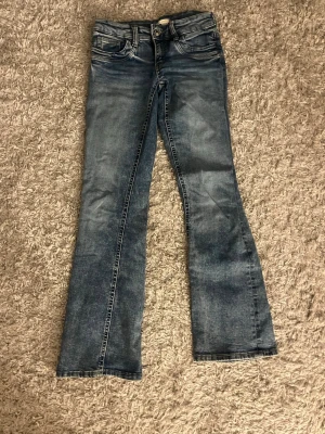bootcut jeans/dżinsy - Säljer ett par blå bootcut jeans med klassiska femficksdetaljer. Jeansen har en låg midja och är tillverkade i denim med lätt stretch. Perfekt för dig som gillar en avslappnad och trendig look.
