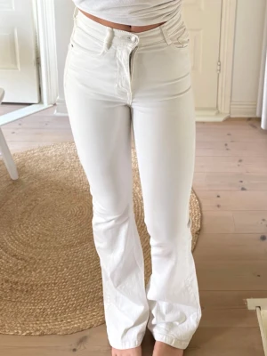 Vita utsvängda jeans med hög midja - Snygga vita jeans med hög midja och utsvängda ben. Jeansen har klassisk femficksdesign och stängs med dragkedja och knapp. Perfekta för en trendig och fräsch look. Materialet är denim med stretch för extra komfort.