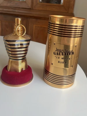 Jean Paul Gaultier Le Male Elixir ca 115 ml kvar - Använd fåtal gånger. Lyxig parfym från Jean Paul Gaultier, Le Male Elixir, i en ikonisk guldfärgad flaska formad som en manlig torso med svarta ränder. Kommer med matchande guldfärgad metalltub och röd sammetsbas. Perfekt för dig som gillar exklusiva dofter och snygg design.