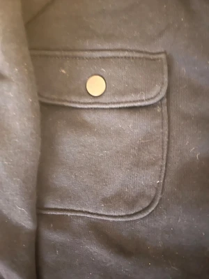 Svart overshirt från Lindex 146-152 - Svart overshirt från Lindex med klassisk krage, två bröstfickor med tryckknappar och raka ärmar. Jackan har en stilren look och är gjord i mjukt bomullsmaterial. Perfekt för lager-på-lager och enkel att matcha med olika outfits. Pris går o diskutera 