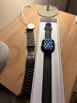 Apple Watch 2025 GPS 46mm Svart - Apple Watch (2025) GPS 46 mm i aluminium med sportband i svart. Klockan har ett sportband, men jag slänger in ett extra band som är stål. Hör av er gärna vid frågor!