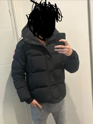 Svart dunjacka från Canada Goose - Säljer en svart dunjacka från Canada Goose med avtagbar pälskrage och klassisk logga på ärmen. Jackan har dragkedja, knappar och flera fickor. Perfekt för kalla vinterdagar och riktigt varm tack vare dunfyllningen. Fick denna jacka i födelsedags present och har nu tagit beslutet till att sälja den då den inte går till någon användning 