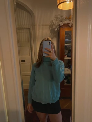 Turkos polotröja i stickat - Mysig turkos stickad polotröja med långa ärmar och ribbade muddar vid ärmslut och nederkant. Tröjan har en hög krage som ger extra värme och en avslappnad passform. Perfekt för kyliga dagar och enkel att matcha med olika outfits. Storleken står att det är XL men skulle absolut säga att det är S