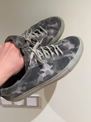 Common projects sneakers - Snygga sneakers i grått camomönster med lågt skaft och matchande grå skosnören. Yttermaterialet ser ut att vara mocka eller textil och sulan är i gummi. Perfekta för dig som gillar streetwear och vill sticka ut lite extra. Nypris är runt 4000kr mitt pris 999