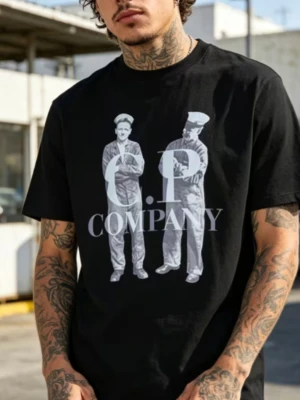 Svart C.P. Company t-shirt - Snygg svart t-shirt från C.P. Company med stort tryck framtill som visar två personer i uniform och tydlig logga. T-shirten har normal passform och är kortärmad, perfekt till en avslappnad streetwear-look. Tillverkad i mjuk bomull för skön känsla.