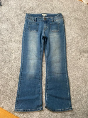 Blå bootcut jeans med fickor - Säljer ett par blå bootcut jeans med två stora framfickor och snygga bakfickor med knappdetaljer!! Jeansen är helt oanvända då dom inte passade 💓💓