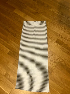 Randig långkjol från Vila - Säljer en lång, vit kjol med svarta tunna ränder från Vila. Kjolen har en rak passform och är gjord i mjukt bomullsmaterial. Perfekt för dig som gillar en enkel och stilren look med klassiska ränder.