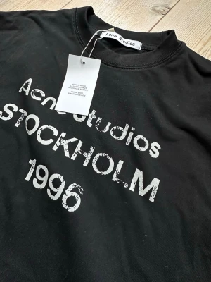 Svart Acne Studios t-shirt med tryck - Svart t-shirt från Acne Studios med vitt tryck på bröstet där det står 'Acne Studios STOCKHOLM 1996'. Klassisk rund hals och korta ärmar. Tillverkad i mjuk bomull för en skön och avslappnad look. Fraktar direkt! Dm vid frågor!