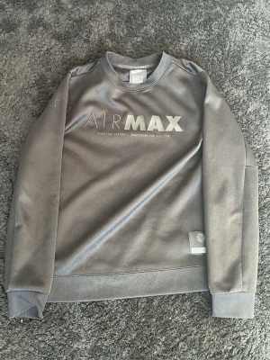 Svart Nike Air Max sweatshirt - Strl L i barnstorlek Snygg svart sweatshirt från Nike med AIR MAX-tryck på bröstet. Tröjan har rund halsringning, långa ärmar och ribbade muddar. Tillverkad i ett mjukt material som känns skönt mot huden. Perfekt för en sportig och avslappnad stil.