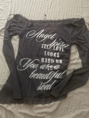 Svart offshoulder topp med spets från new yorker - Trendig svart offshoulder topp med spetsdetaljer upptill och nedtill. Långärmad modell med texttryck framtill. Perfekt för dig som gillar statement-plagg. Den har scrunch på ena sidan vilket gör att den har jättefin passform. Storlek M men skulle nog snarare säga S. Den går grå/svart men satte grå i beskrivningen. 