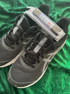 Svarta Asics sneakers i mesh St.39 - Säljer ett par svarta Asics sneakers med ovandel i ventilerande mesh och klassisk snörning. Skorna har vita detaljer och en bekväm sula som passar perfekt till streetwear eller träning. Stilren design och riktigt sköna på foten.