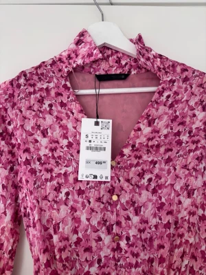 Rosa blommig kortklänning med knappar -  Rosa kortklänning från Zara  med blommigt mönster i olika rosa nyanser. Perfekt för vår och sommar. Helt ny och säljer endast då den inte kommer till användning.💓☀️ 