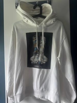 REPLAY Hoodie - * Vit hoodie från Replay med en ren och modern design. * Distinkt svart grafiskt tryck på bröst/mage med två utsträckta händer som skapar ett starkt visuellt uttryck. * Tillverkad för hög komfort med en avslappnad och stilren passform. * Klassiska detaljer såsom huva, ribbade muddar och känguruficka. * Ett exklusivt streetwear-plagg som kombinerar kvalitet, design och karaktär. * Perfekt för dig som söker en trendmedveten hoodie med en unik och iögonfallande design.