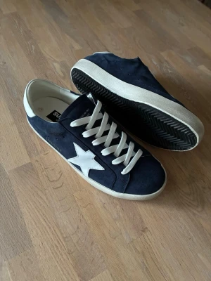 Golden goose superstar navy blå - Säljer ett par navy blåa golden goose superstar skor. Skorna har snygga slitningar och har navy blå mocka. Skorna är av storlek 43 och formar sig bra över tid. Skorna är även oanvända