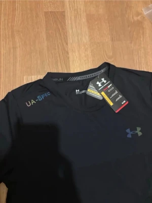 Svart träningsset från Under Armour - Snyggt svart träningsset från Under Armour med t-shirt och shorts. Setet har diskreta regnbågsfärgade logotyper och textdetaljer. Tillverkat i lätt och snabbtorkande material, perfekt för löpning eller gym. Klassisk passform och elastisk midja på shortsen.
