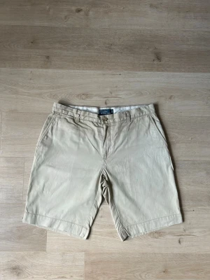 Beiga Ralph Lauren Chinos Shorts Chinosshorts Storlek W34 - Mycket fina Ralph Lauren shorts i beige färg | Jeansen är i mycket bra skick och sparsamt använda. |  Äkta som allt annat jag säljer! ✅ |  Storlek: W34 | Skick: Mycket Bra Skick - Har tyvärr några väldigt små fläckar (SE SISTA BILDER) | Färg: Beige | Märke: Ralph Lauren| Modell: Shorts |   Hör gärna av dig vid frågor så svarar jag så fort jag kan! 😁 |  (SKU - 181)