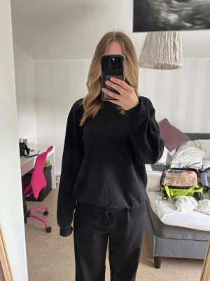 Svart basic sweatshirt - En enkel svart sweatshirt med rund hals och långa ärmar. Tröjan har ribbade muddar vid ärmslut och nederkant. Perfekt för en clean och avslappnad stil. Materialet ser ut att vara mjuk bomullsblandning.
