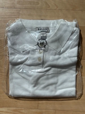 Vit pikétopp från Van Heusen - Klassisk vit pikétopp från Van Heusen med krage och tre knappar framtill. Tillverkad i mjuk bomull som känns skön mot huden. Enkel och stilren design som passar till många olika looks.