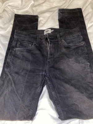 Svarta raka jeans från 157 - Tvättar med textilfärg för att få tillbaka den svarta färgen!! Säljer ett par svarta jeans från 157 med klassisk femficksmodell och raka ben. Jeansen har bälteshällor, knappgylf och diskret svart patch bak i midjan. Materialet är denim i bomull med en något tvättad look.