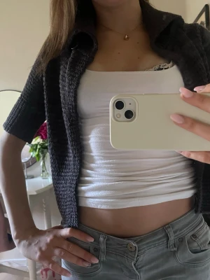 Mörkgrå stickad kortärmad kofta - Kortärmad stickad kofta i mörkgrått med krage och knapp framtill. Modellen är något croppad och har en öppen front som kan stängas med en knapp vid halsen. Skriv gärna om ni har fler frågor💞
