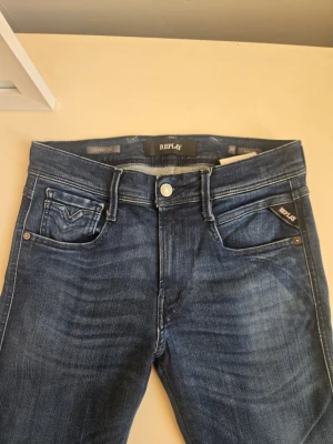 Blå slim fit jeans från Replay - Snygga blå slim fit jeans från Replay med klassisk femficksdesign och subtila slitningar. Jeansen har normal midja, dragkedjegylf och Replay-logga på myntfickan. Perfekta för en trendig och avslappnad stil.