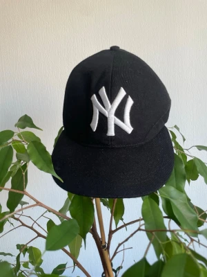 Vintage Keps - Säljer en svart keps från New Era med klassiskt New York Yankees-broderi i vitt framtill. Kepsen har böjd skärm och justerbar baksida. Tillverkad i bomullstyg och passar perfekt till streetwear-stilen.