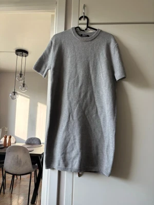 Grå stickad kortklänning Gina Tricot - Mysig grå stickad kortklänning från Gina Tricot med rund halsringning och korta ärmar. Perfekt för lager på lager och enkel att styla med accessoarer. Mjuk och bekväm känsla i materialet.