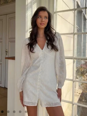 Embroidery dress - Kort klänning med långa ballongärmar. Klänningen är vit och har broderidetaljer. Den har knappar ner längs framsidan, figurnära passform och v-ringning.  Helt nyskick och använd en gång, nypris var 400kr säljes för 270, finns på ginas hemsida som ”embroidery dress”  den är i offwhite.       hör av er för mer bilder eller vid frågor!🥰