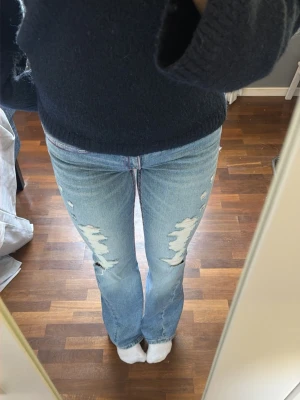 Ljusblå bootcut jeans - Säljer ett par ljusblå bootcut jeans med slitningar framtill och broderade detaljer i rosa på bakfickorna. Jeansen är low waist, och jag är 169cm lång. Jeansen är endast använda 2 gånger. Kom privat för mer info☺️