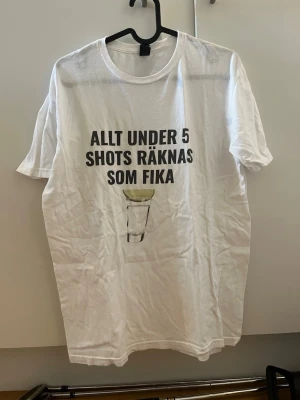 Vit t-shirt med shots-tryck - Vit t-shirt från merchoteket.se perfekt för sommar fester, använd en gång sen legat i garderoben ett bra tag