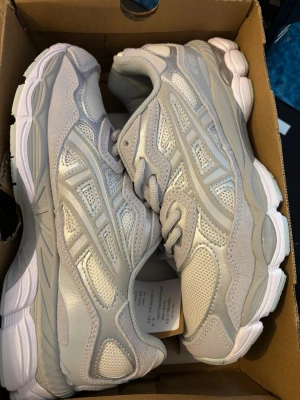Grå Asics sneakers med mesh och mocka - Snygga sneakers från Asics i ljusgrå färg med detaljer i mesh och mocka. Skorna har en chunky sula i vitt och klassisk Asics-logga på sidan. Perfekta för dig som gillar sportig och clean stil. Lågt skaft och sköna att bära hela dagen.