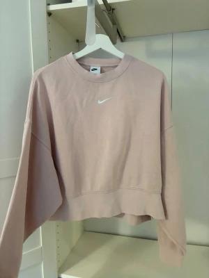 Ljusrosa croppad sweatshirt Nike - Ljusrosa croppad sweatshirt från Nike med klassisk vit logga på bröstet. Tröjan har en loose passform och långa ärmar. Nypris ca 500 kr. 
