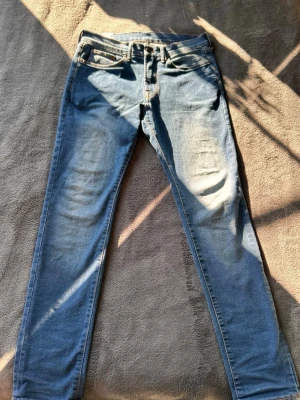 Blå skinny jeans  - Säljer ett par klassiska blå skinny jeans med fem fickor och orangea kontrastsömmar. Jeansen har normal midja och är tillverkade i stretchigt denimtyg för en bekväm passform. Perfekta till en avslappnad stil och lätta att matcha med olika plagg.