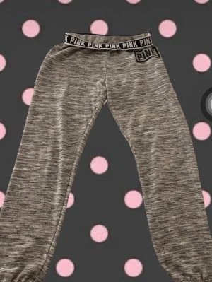 Grå mjukisbyxor från PINK - Säljer ett par gråmelerade mjukisbyxor från PINK med bred resår i midjan där det står 'PINK' runtom. Byxorna har avslappnad passform och tryckt logga längs ena benet. Perfekta för chill dagar och riktigt sköna att ha på sig.