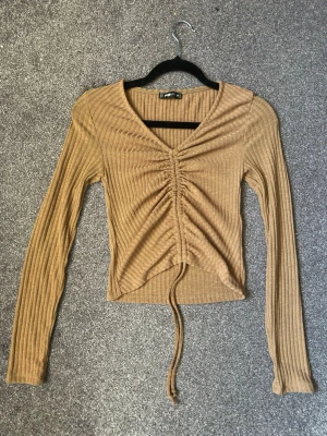 Ribbad brun långärmad topp med snörning - Trendig ribbad brun topp från Bershka med lång ärm och v-ringning. Toppen har snygg snörning framtill som ger en cool rynkad effekt och croppad passform. 