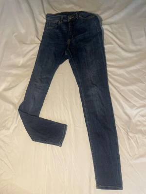 Mörkblå skinny jeans med kontrastsömmar  - Säljer ett par mörkblå skinny jeans med klassisk femficksdesign och snygga kontrastsömmar. Jeansen har normal midja och är tillverkade i ett stretchigt denimtyg som sitter tajt längs benen. Från Monki