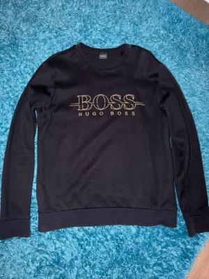 Hugo Boss - Snygg svart sweatshirt från Hugo Boss. Tröjan har rund halsringning och långa ärmar. Storleken är L men den passar mer som en S