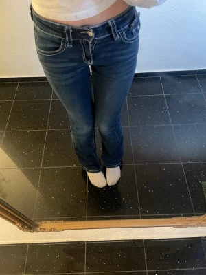 Mörkblå bootcut jeans - Säljer ett par mörkblå bootcut jeans med vita kontrastsömmar och låg midja. De är i storlek 158!