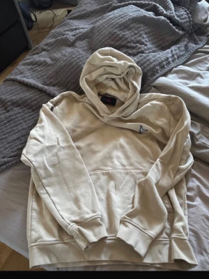 Beige hoodie från Jordan - Snygg beige hoodie från Jordan med klassisk logga broderad på bröstet. Hoodien har en stor huva och magficka, samt ribbade muddar vid ärmar och nederkant. Tillverkad i mjukt material som känns skönt mot huden. Perfekt för en avslappnad streetwear-look.