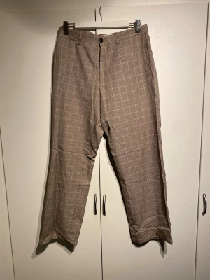 Beige rutiga kostymbyxor från Topman - Snygga beige kostymbyxor med diskret rutigt mönster från Topman. Byxorna har normal passform, raka ben och klassisk midja. Perfekta för en stilren look och passar till skjorta eller t-shirt. Materialet känns lätt och bekvämt. Storlek 32 32 och true to size.